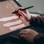 A man working on a graphic tablet. He holds a stylus in his right hand and draws and edits an image
