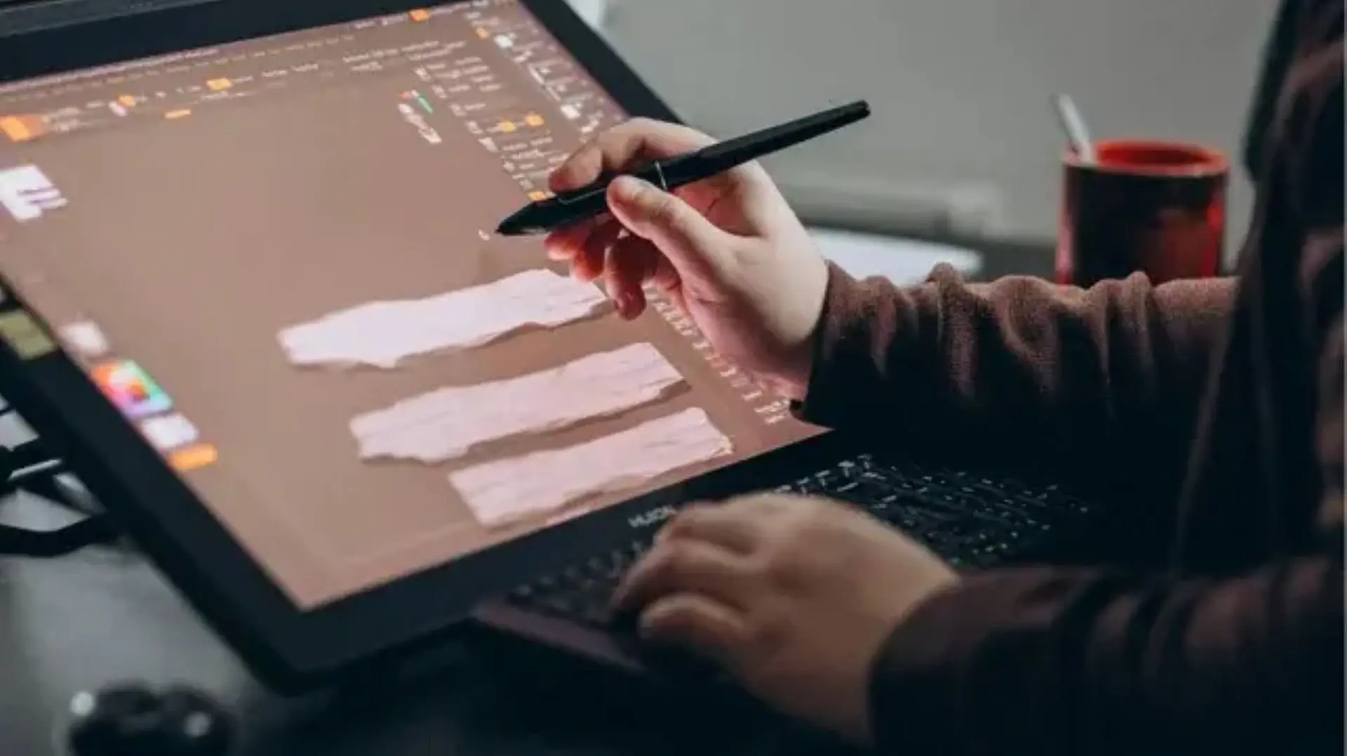 A man working on a graphic tablet. He holds a stylus in his right hand and draws and edits an image